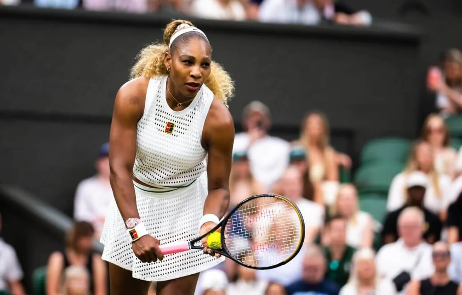 Serena Williams prepares to serve on a tennis court wearing a breathable Nike tennis outfit.
