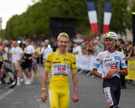 Tadej Pogacar in yellow jersey and Isaac Del Toro in white jersey stand on a road with French flags behind them
